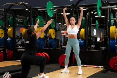 woman lifts a barbell with a personal trainer